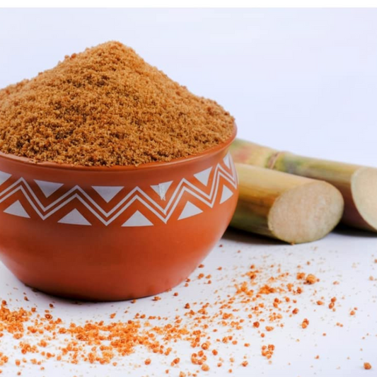 Prakriti Organics organic jaggery powder in a decorative bowl with sugarcane pieces in the background