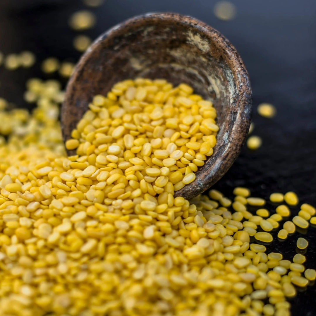 Organic yellow moong dal spilling from a rustic bowl onto a dark surface