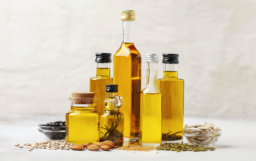 Collection of organic cooking oils in various bottles with seeds and nuts on a light background