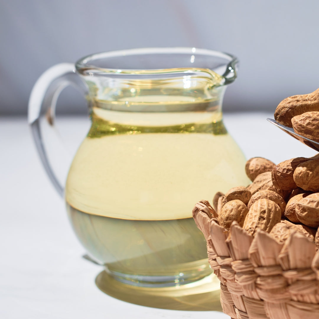 Cold pressed groundnut oil in a clear glass jug next to freshly harvested groundnuts