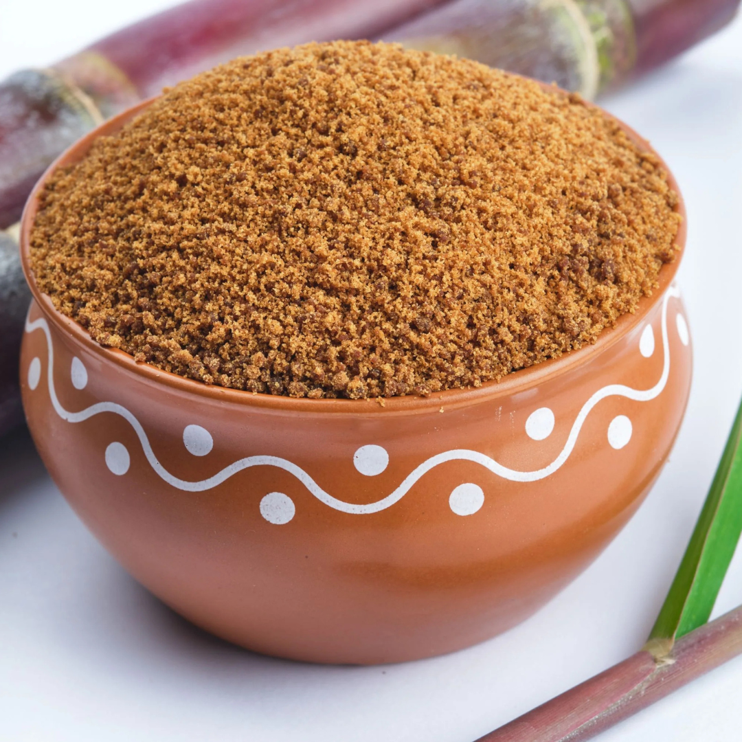 Prakriti Organics organic jaggery powder in a clay bowl with fresh sugarcane stalks in the background