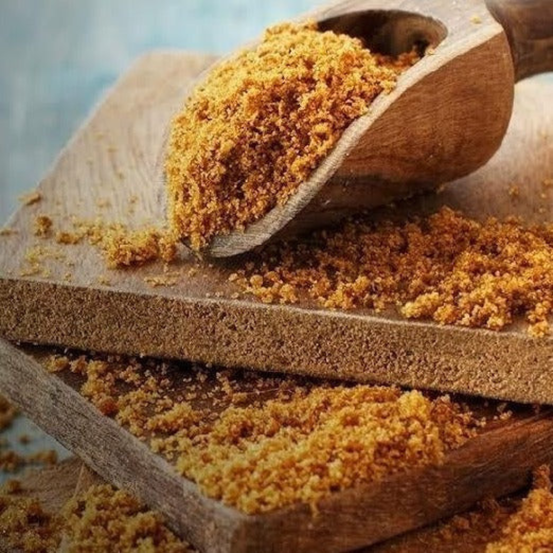 Prakriti Organics organic jaggery powder in a wooden scoop on textured wooden surface