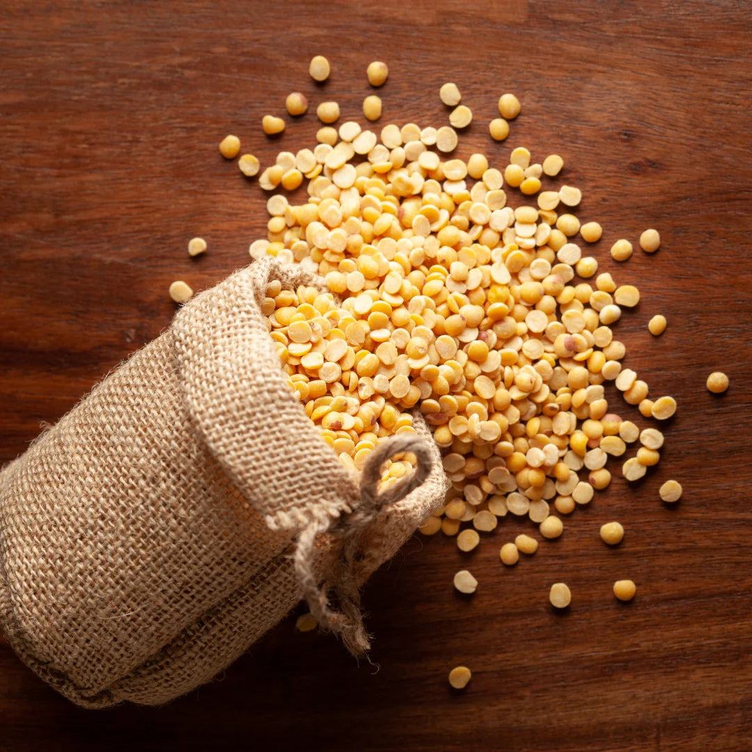 Sack of organic tur dal spilled on wooden surface, showcasing high-quality lentils for cooking.