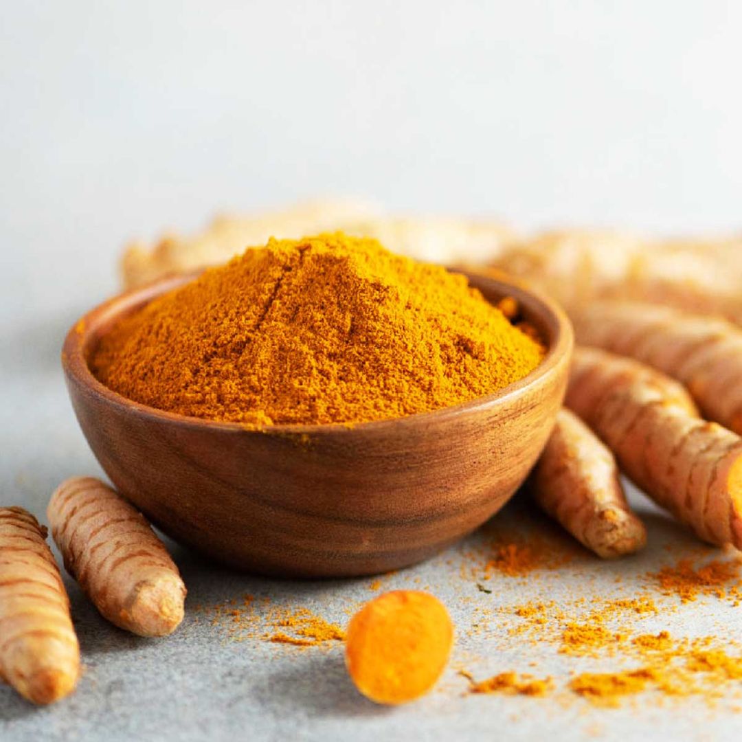 Organic turmeric powder in a wooden bowl with fresh turmeric roots for healthy cooking